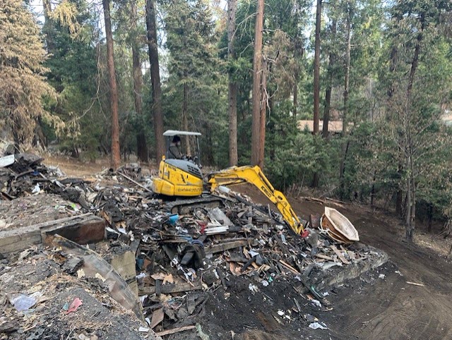 Excavator clearing a fire-damaged house in Crestline